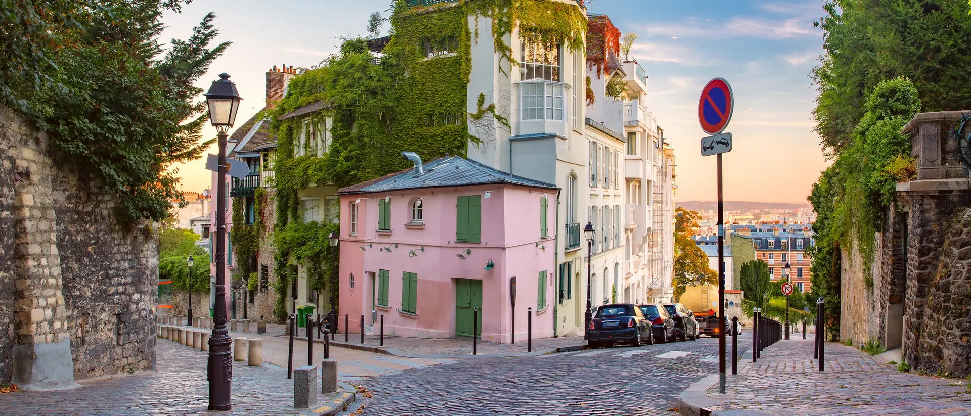 A charming cobblestone street in a picturesque neighborhood with lush greenery and pastel-colored buildings.