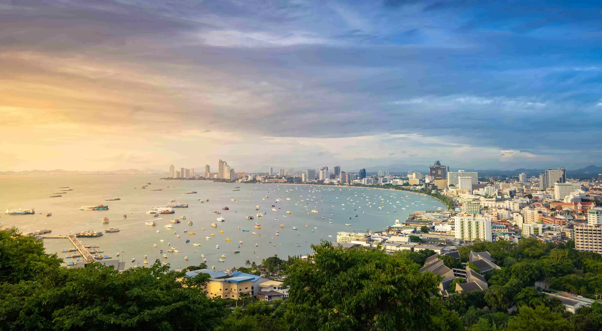 Bang Lamung District Arieal sunset view of boats in water and buildings along curved coastline of Pattaya city