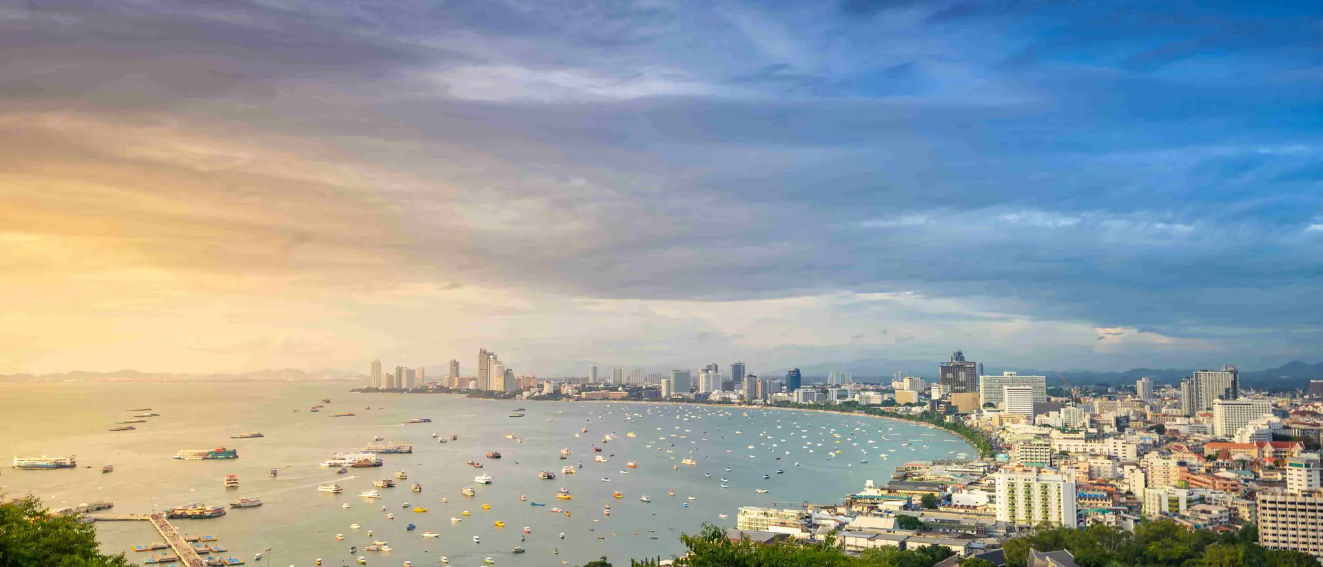 Bang Lamung District Arieal sunset view of boats in water and buildings along curved coastline of Pattaya city