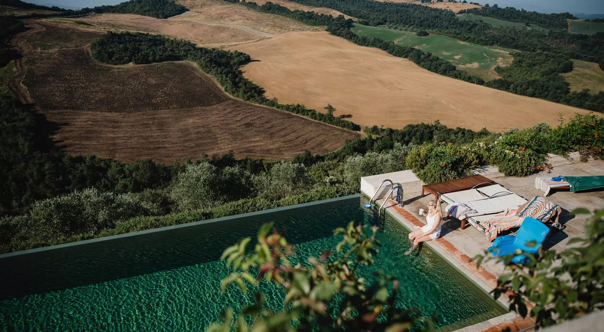 A serene outdoor setting with a pool overlooking rolling hills and farmland, as a person relaxes by the water.