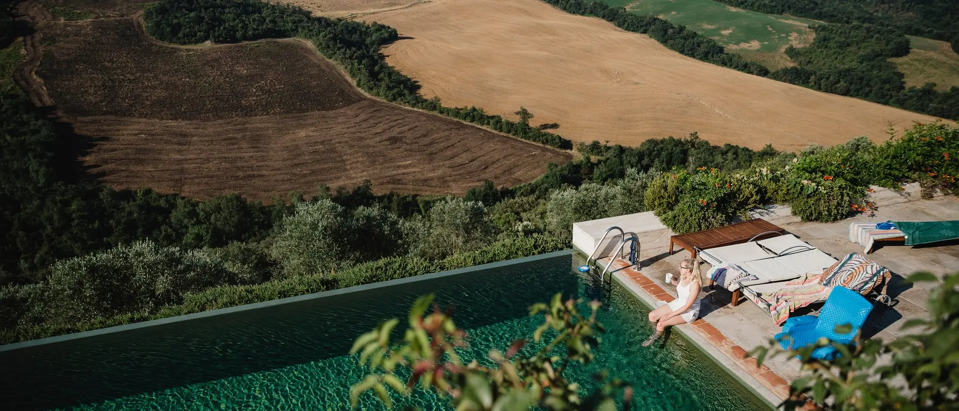 A serene outdoor setting with a pool overlooking rolling hills and farmland, as a person relaxes by the water.