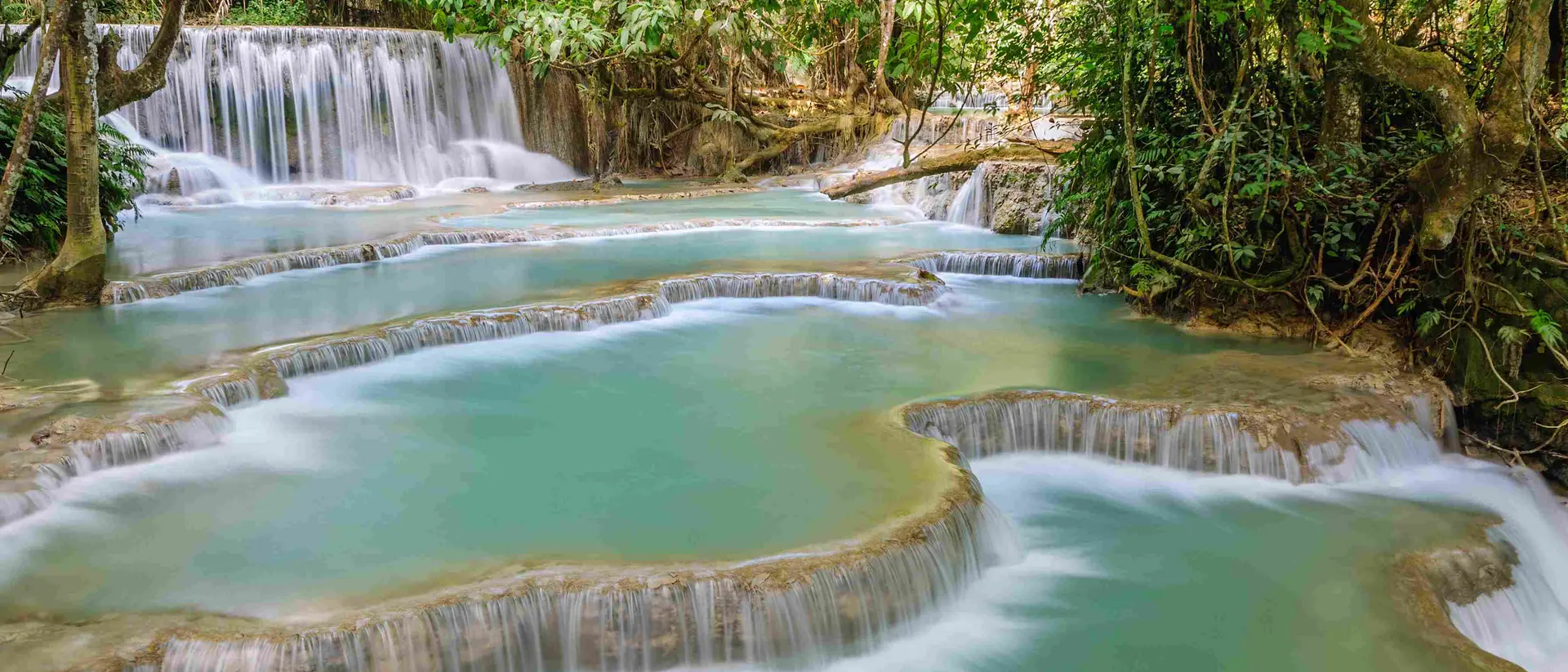 The Kuang Si Falls begin in shallow pools atop a steep hillside. The water flows in to a turquoise blue pool