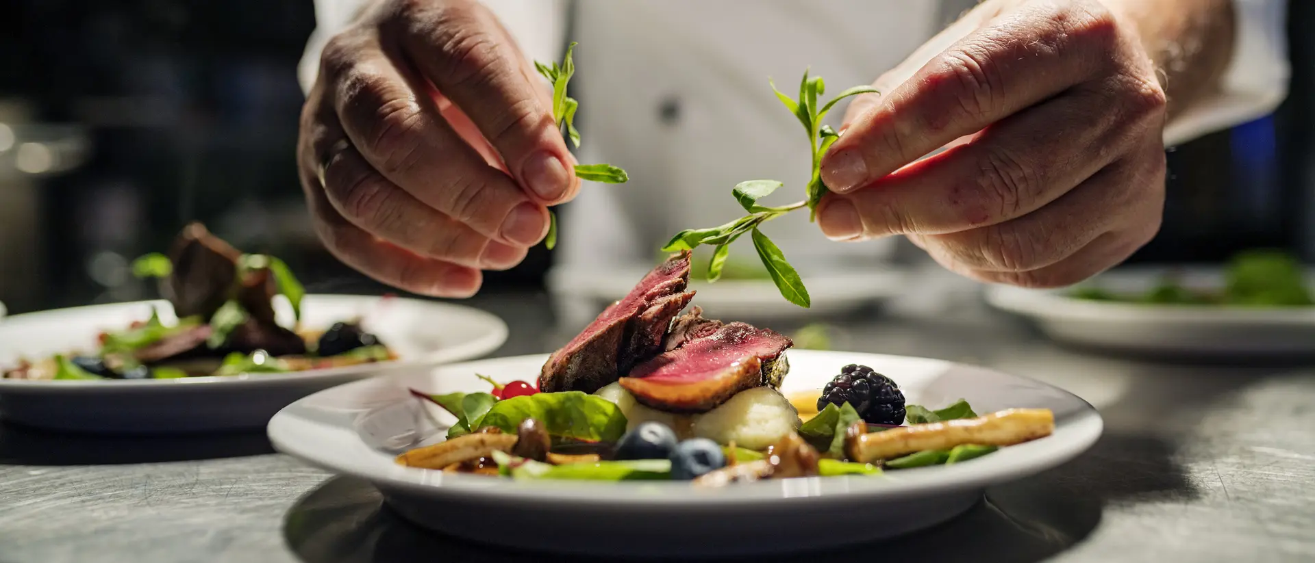 Chef garnishing a beautifully plated dish with fresh herbs in a restaurant kitchen.