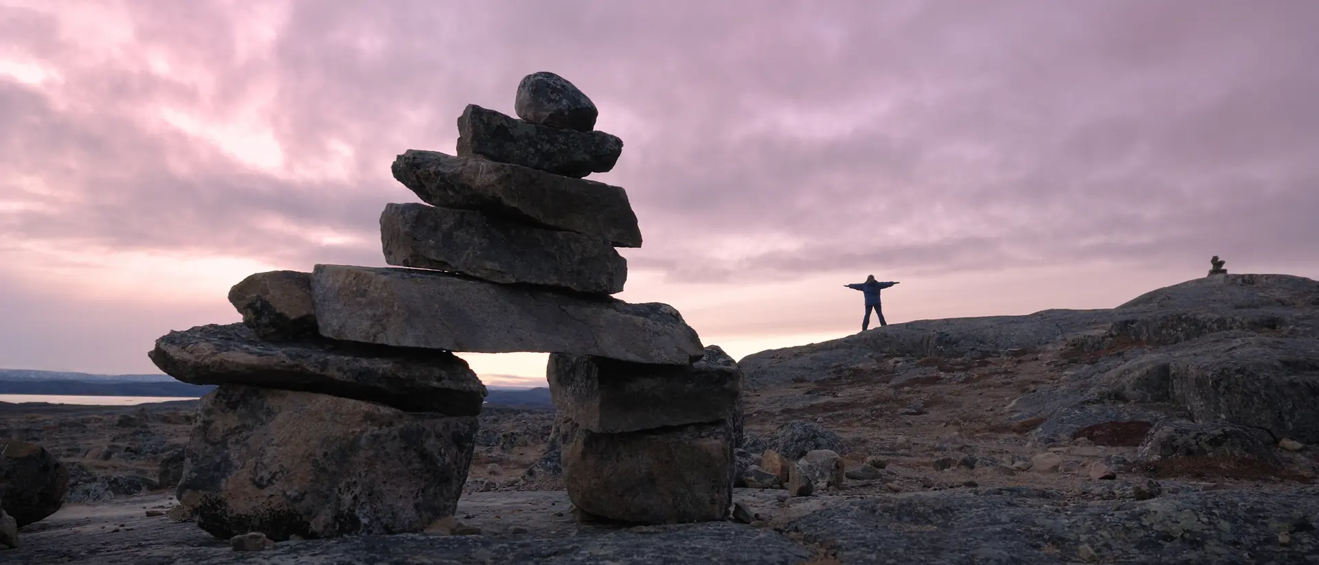 Several inukshuks and a woman becoming one in a beautiful arctic sunset.