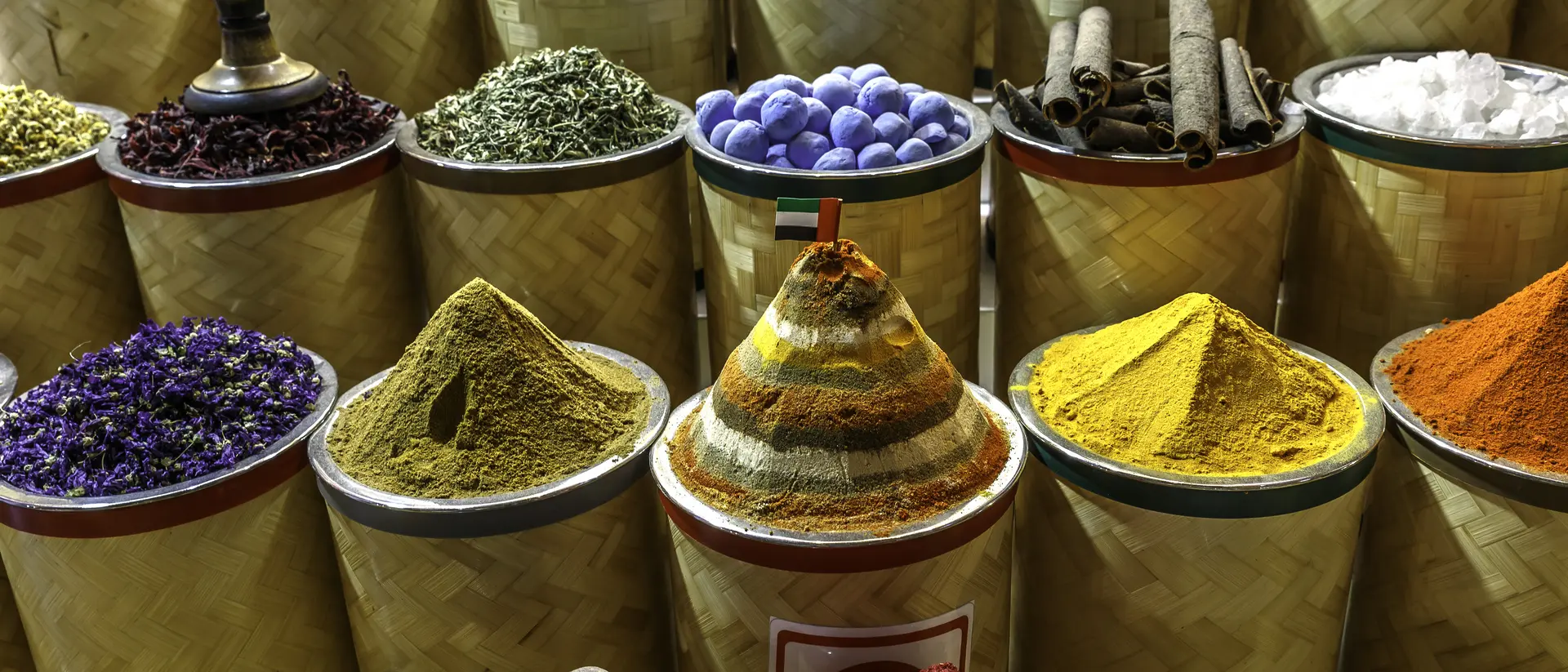 Colorful spices and herbs in cylindrical containers, arranged in rows, showcasing various textures and vibrant hues.
