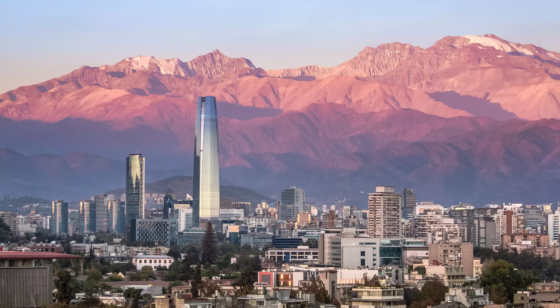 Sunset over a city skyline with modern buildings and mountains in the background.