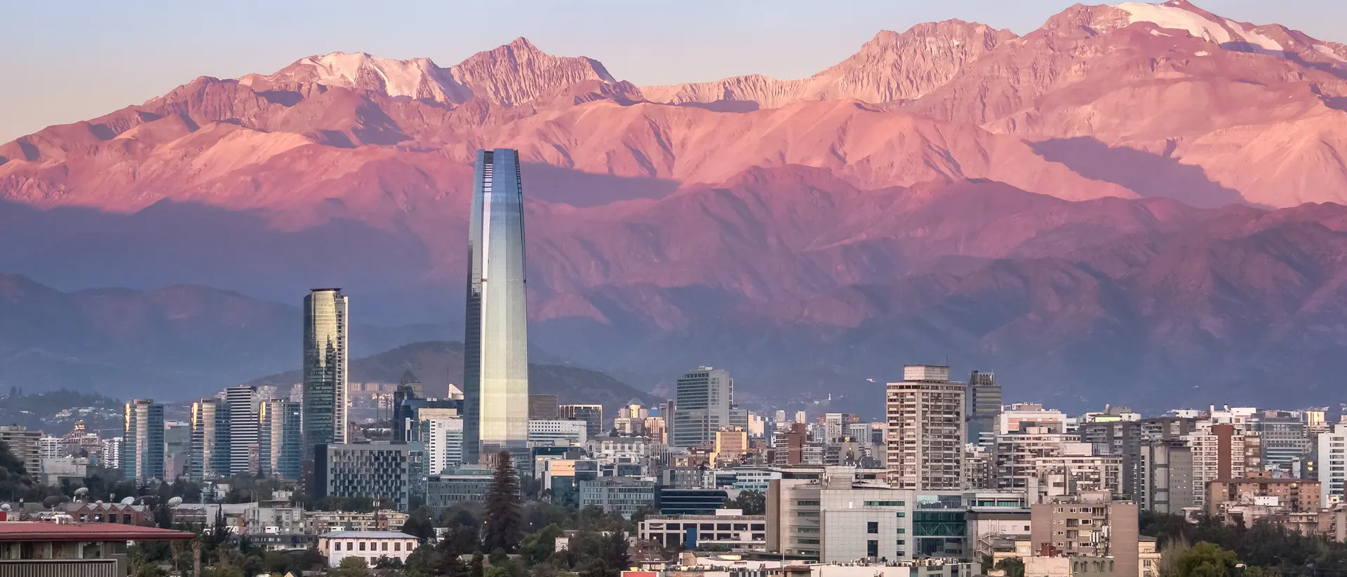 Sunset over a city skyline with modern buildings and mountains in the background.