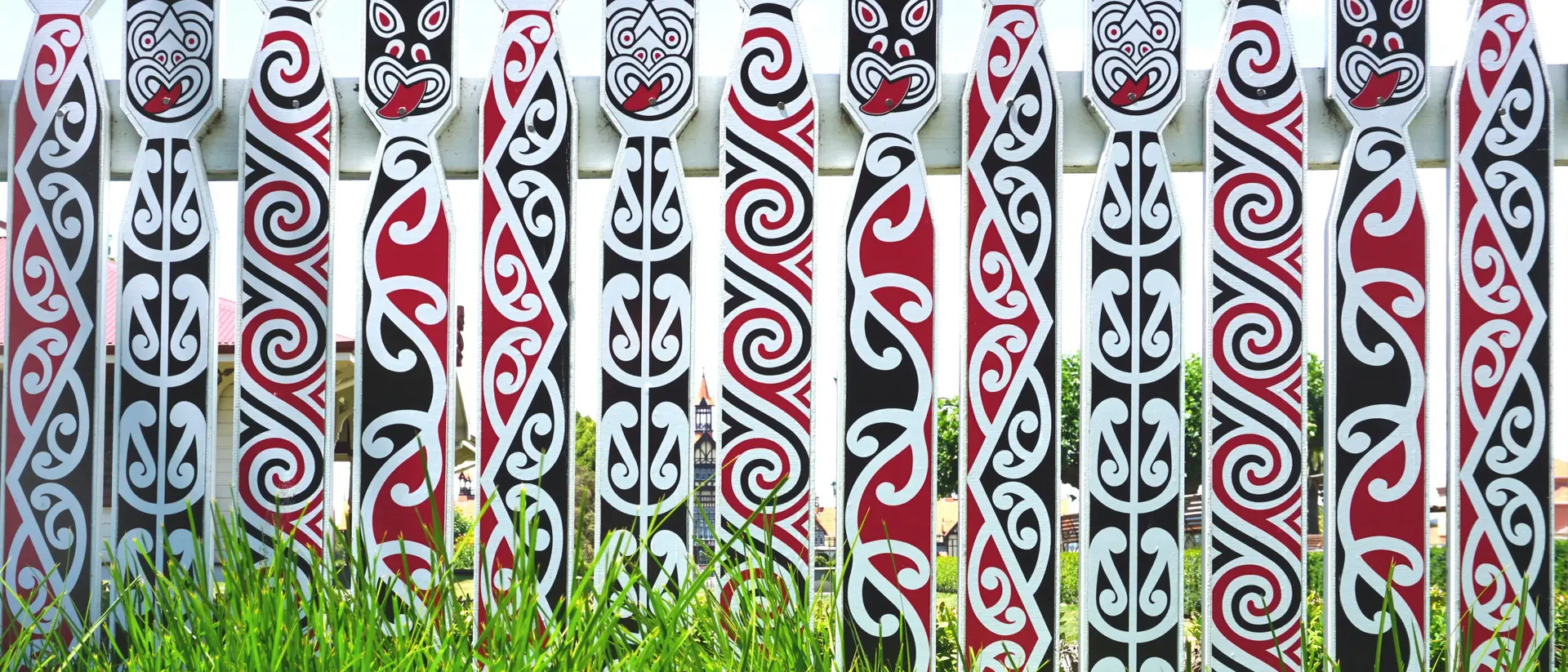 A row of decorated totem poles with intricate tribal patterns in black, red, and white, set against green grass.