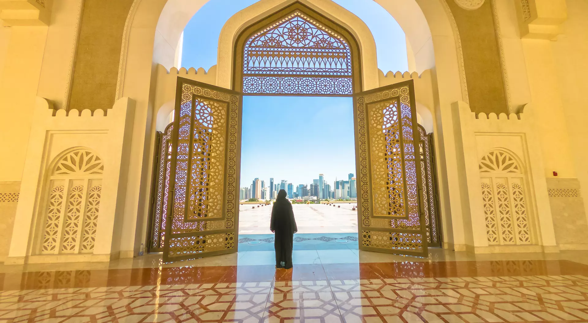 A person stands at an ornate doorway, overlooking a city skyline under a clear blue sky.