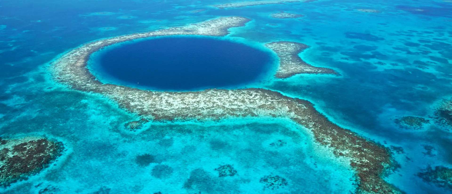Aerial view of a large blue hole surrounded by turquoise waters and coral reefs.