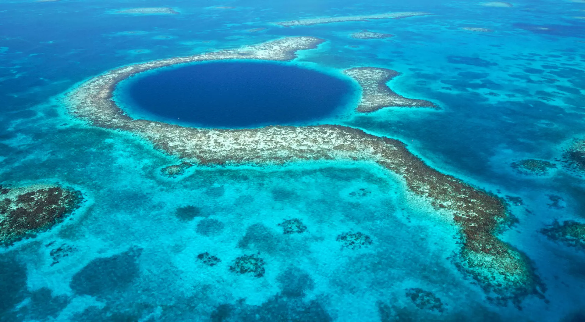 Aerial view of a large blue hole surrounded by turquoise waters and coral reefs.