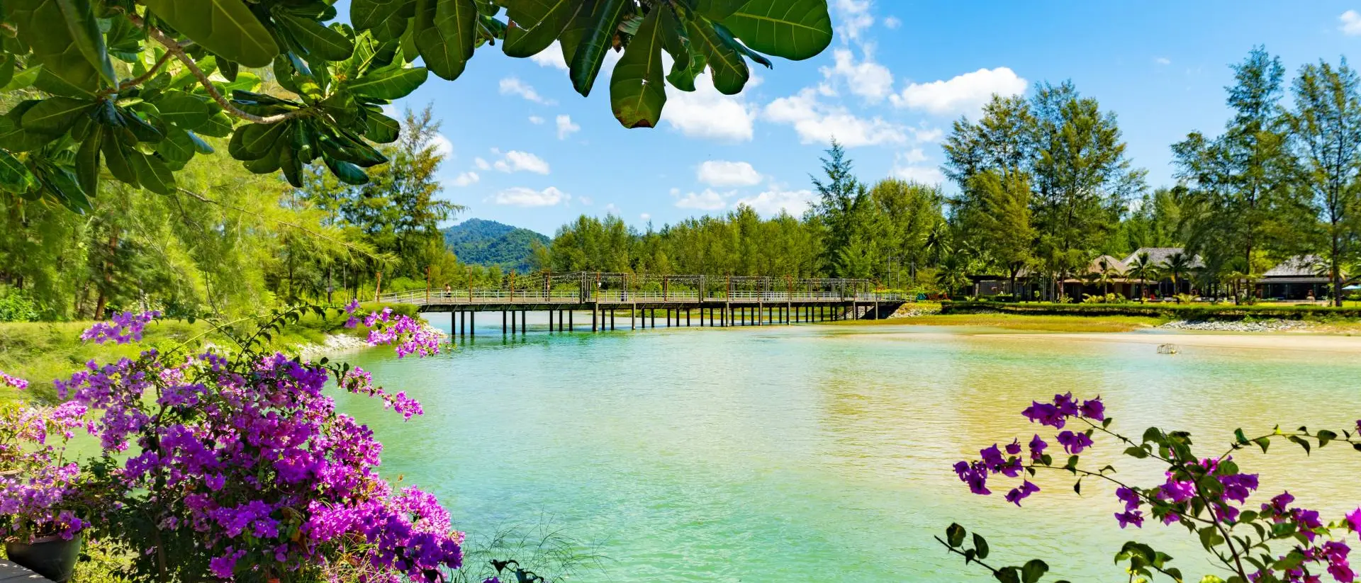 Apsara Beach Resort, Khao Lak, Takua Pa, Phang-nga Bridge between two sides of the beach. There are flowers and palm trees in a formal garden in the foreground