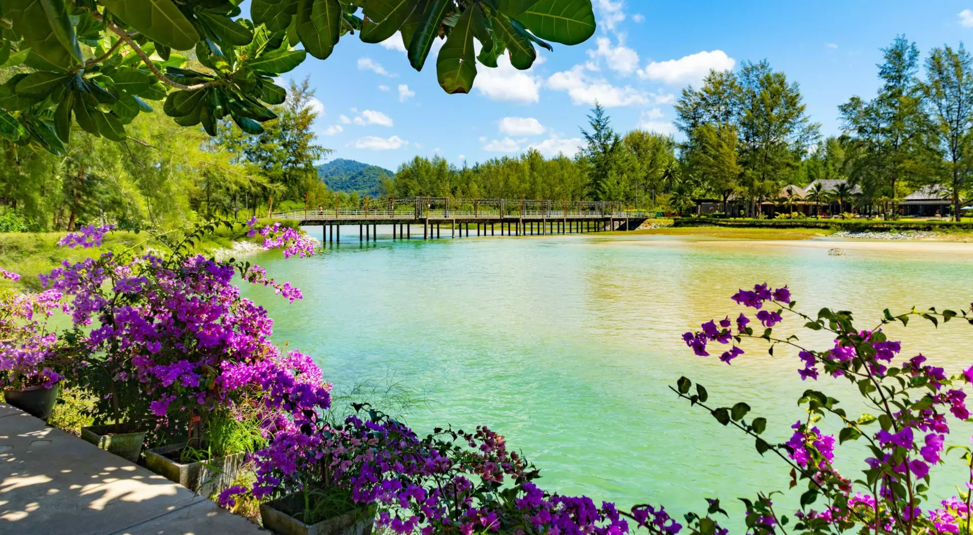 Apsara Beach Resort, Khao Lak, Takua Pa, Phang-nga Bridge between two sides of the beach. There are flowers and palm trees in a formal garden in the foreground