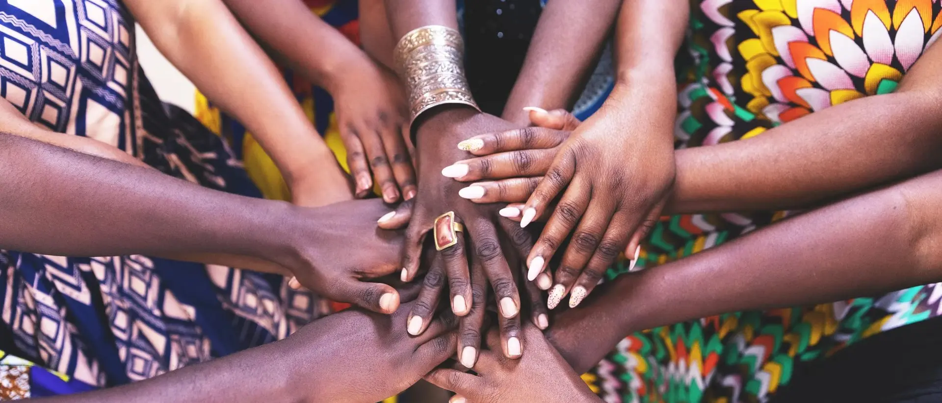 A circle of diverse hands overlapping each other, showcasing unity and collaboration with colorful patterns in the background.