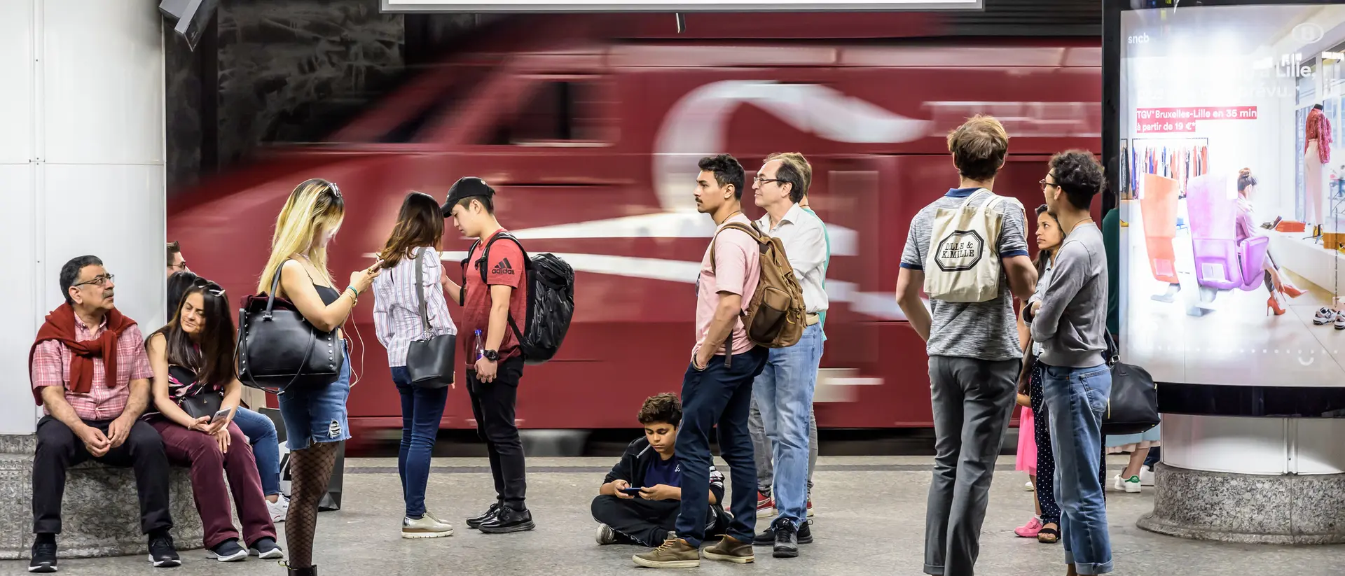 A busy train station platform at Bruxelles Central, with passengers waiting and a train passing in the background.