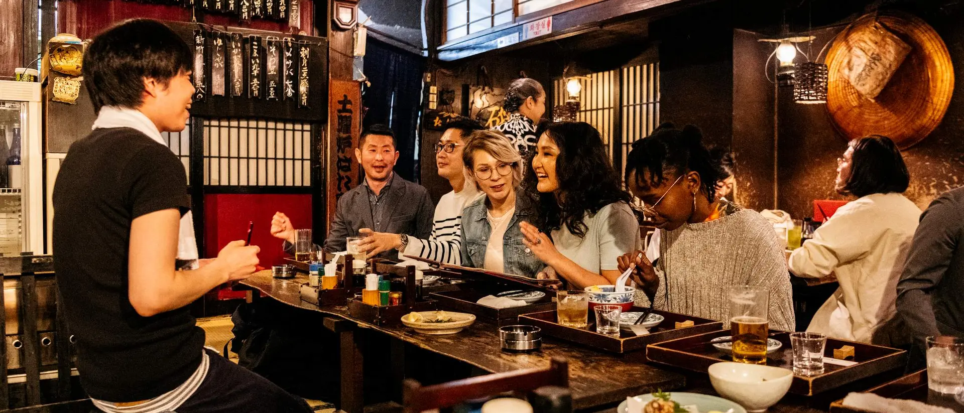 Group of friends dining together in a cozy restaurant, enjoying food and drinks, with warm lighting and traditional decor.