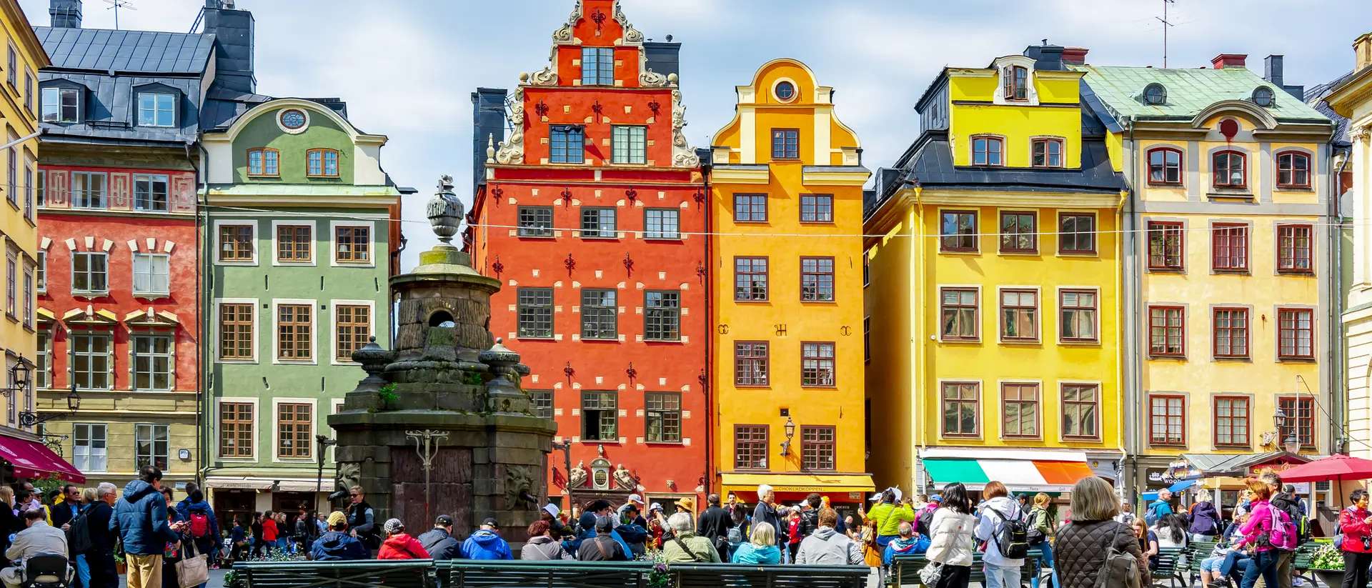 A vibrant square filled with people surrounded by colorful historic buildings under a cloudy sky.