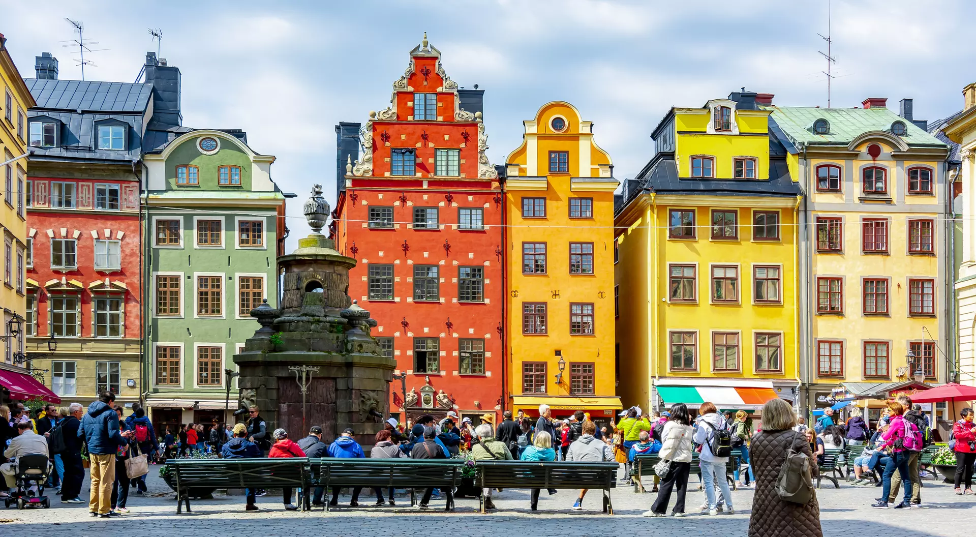 A vibrant square filled with people surrounded by colorful historic buildings under a cloudy sky.