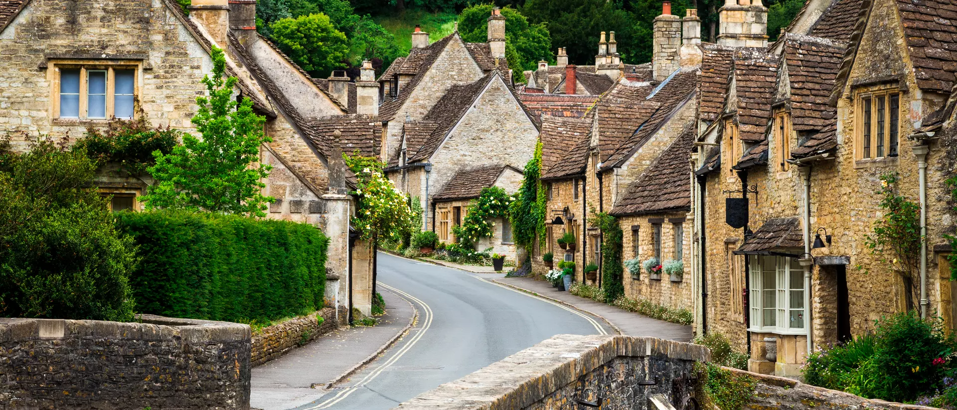 Traditional English village in the Cotswolds area of southwest England. The cosy little brick cottages line the narrow road, and there is also a quaint bridge spanning a little stream.