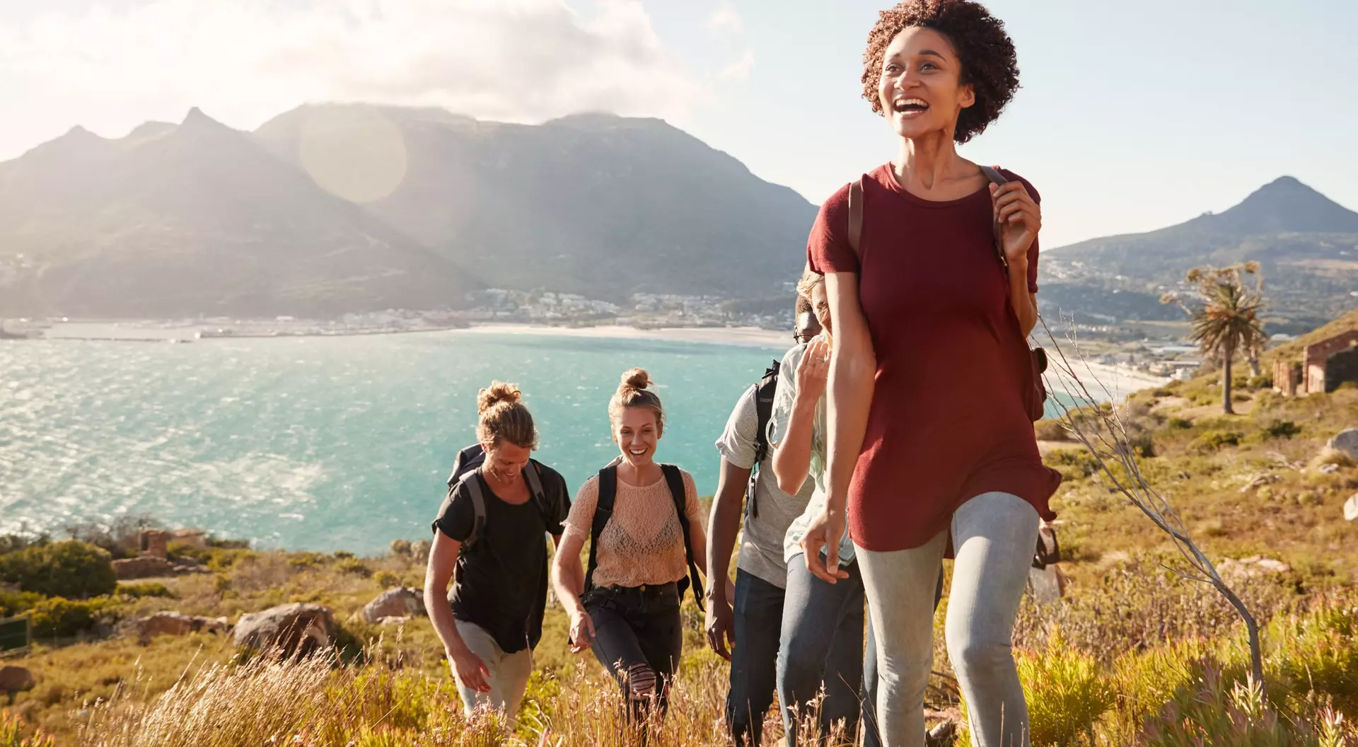A group of friends hiking together with mountains and the sea in the background, enjoying a sunny day outdoors.