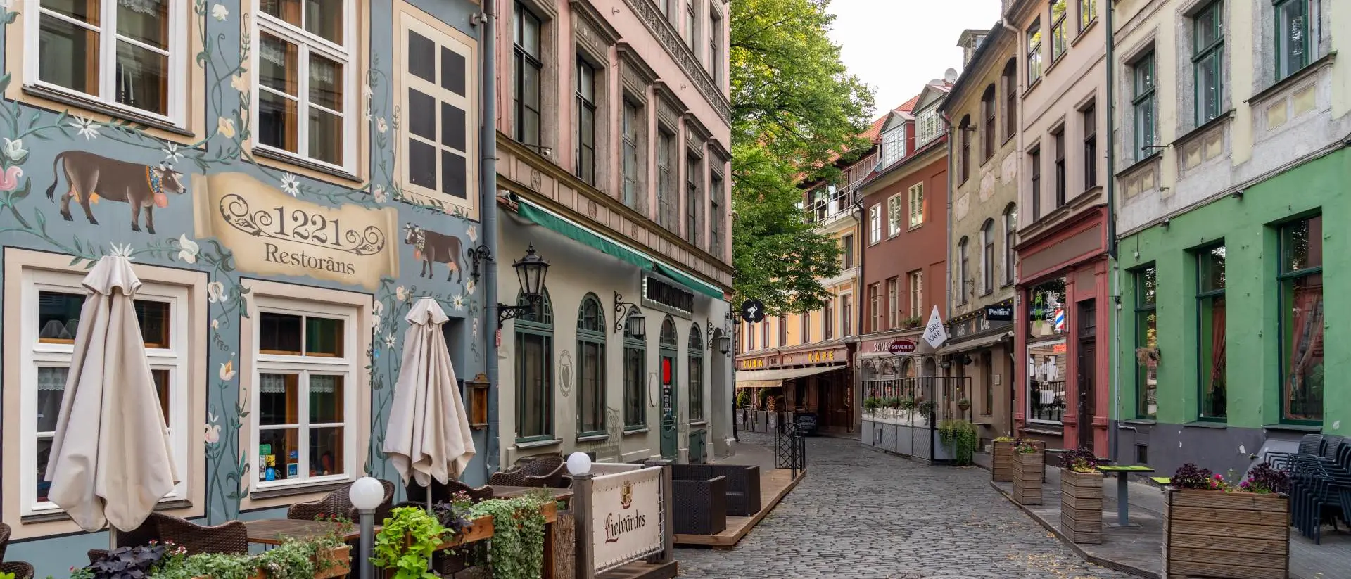 Charming cobblestone street lined with colorful buildings and outdoor restaurant seating under clear skies.