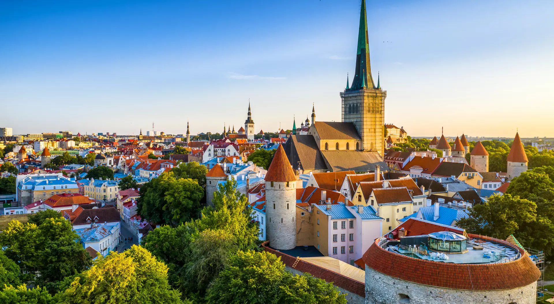 A scenic view of Tallinn's historic skyline with colorful rooftops and a prominent church spire under a blue sky.