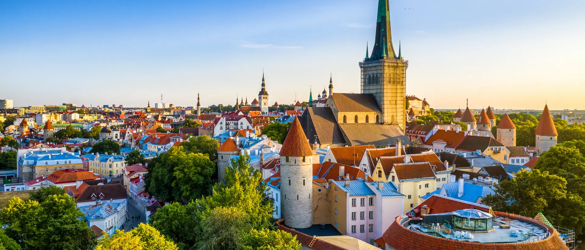 A scenic view of Tallinn's historic skyline with colorful rooftops and a prominent church spire under a blue sky.