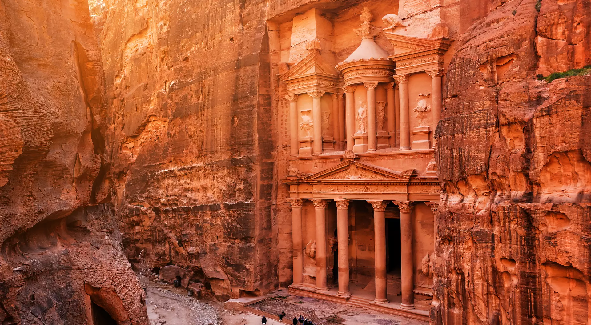 Petra's Treasury in a canyon, illuminated by golden sunlight, with visitors admiring the ancient rock-cut architecture.