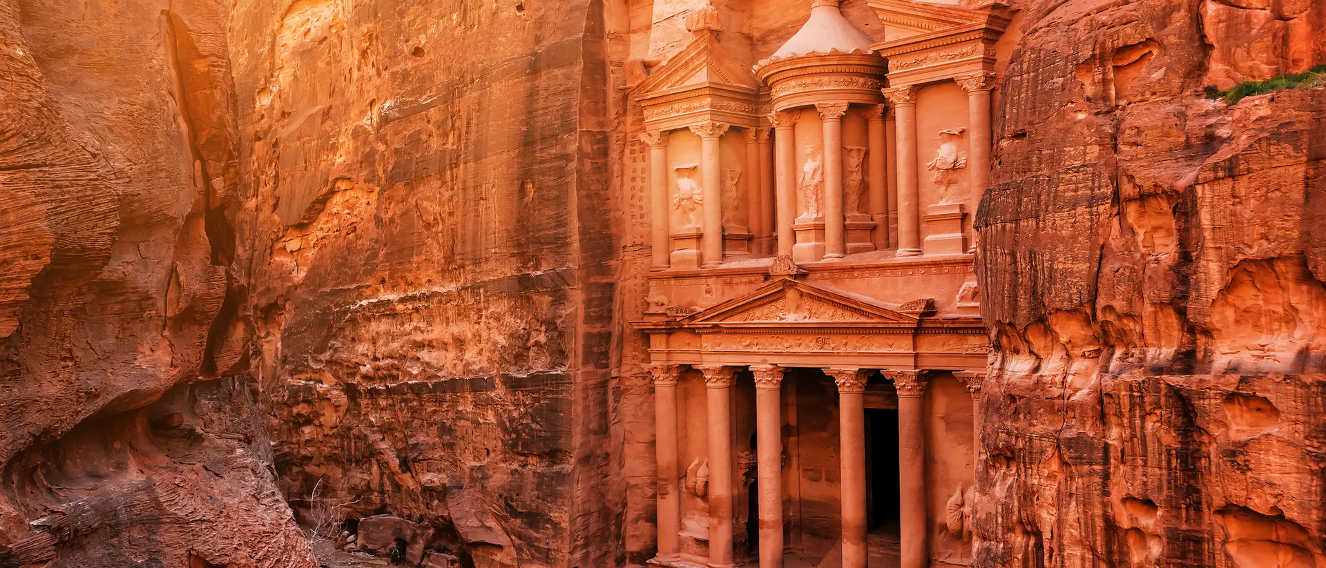 Petra's Treasury in a canyon, illuminated by golden sunlight, with visitors admiring the ancient rock-cut architecture.