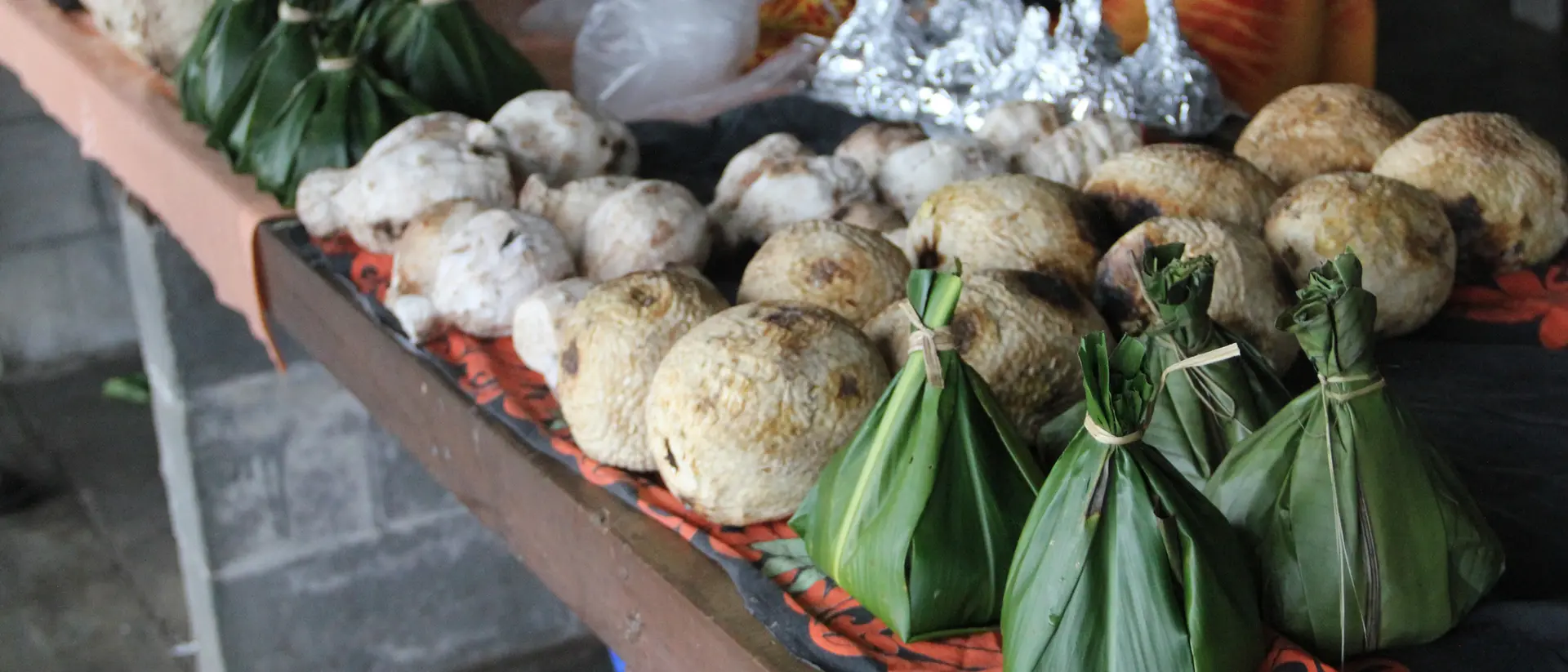 A market stall displays various food items, including round dumplings and bundled parcels wrapped in green leaves.