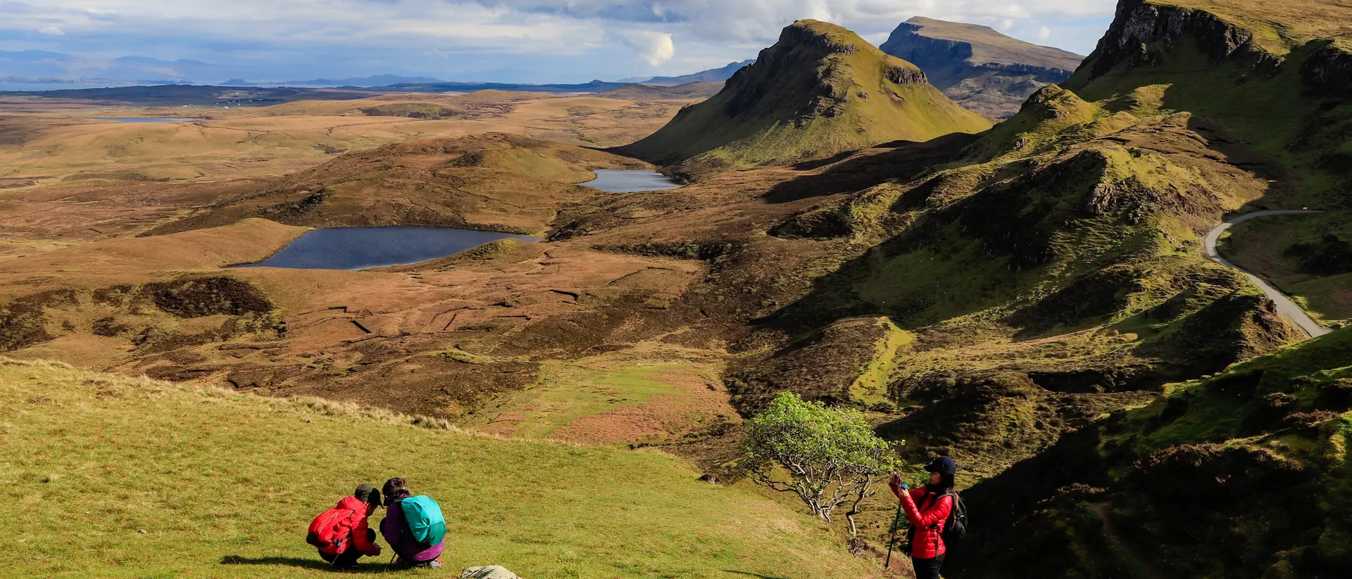Two hikers explore a rocky hillside with a panoramic view of distant mountains and a tranquil landscape.
