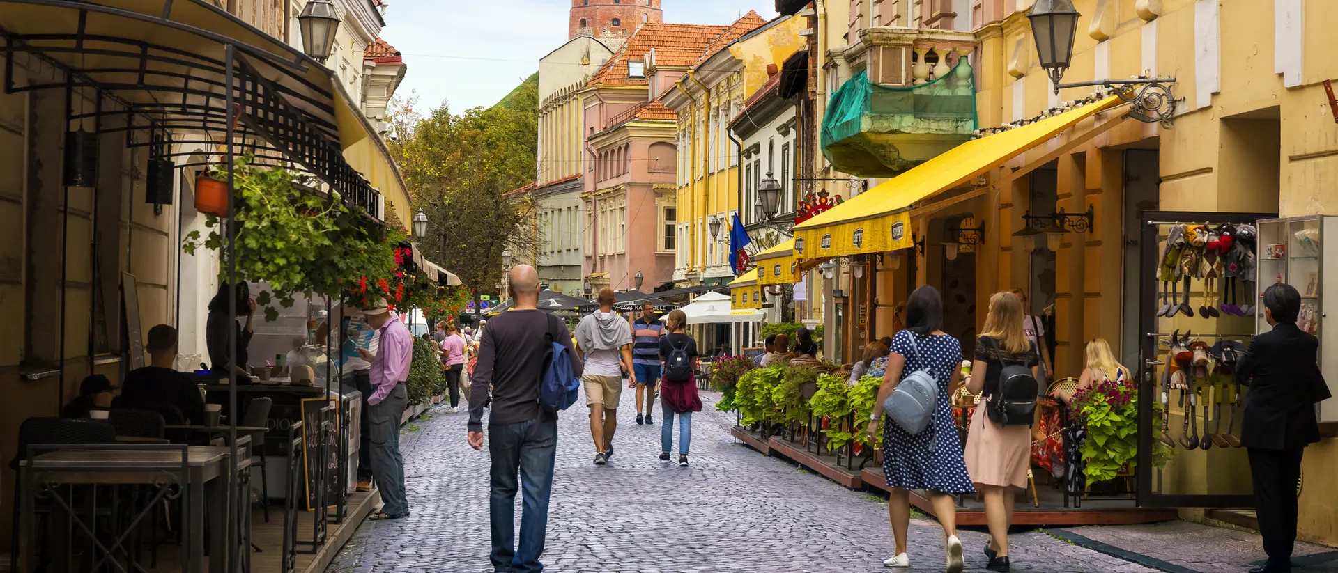 Charming cobblestone street lined with shops and cafes, bustling with pedestrians under a blue sky.