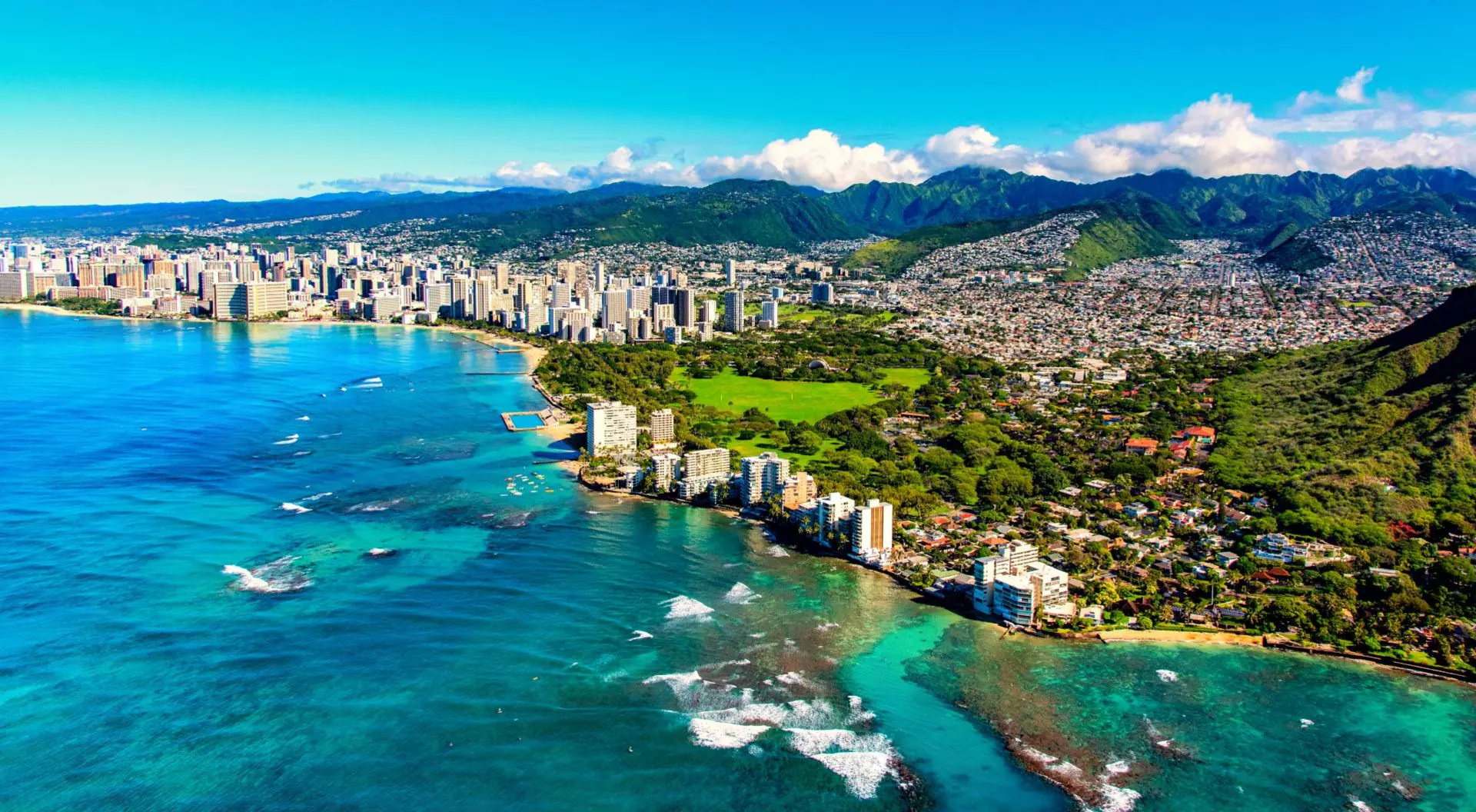 The entire coastline including the base of Diamond Head crater and state park, past the hotel lined Waikiki Beach towards downtown in the distance including the suburban neighborhoods dotting the hills surrounding the city center.