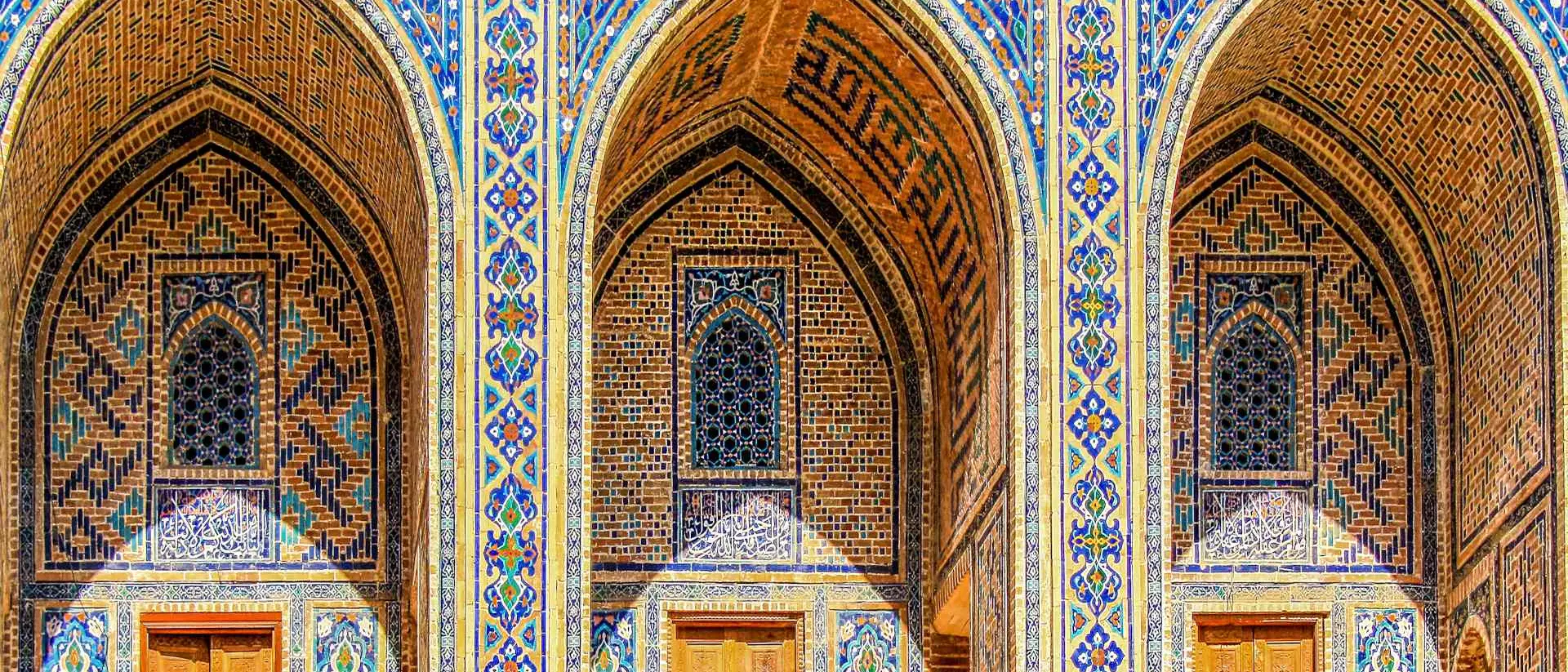 Sherdor Madrassah facade with blue, yellow and green tiles, wall with tall arches and windows