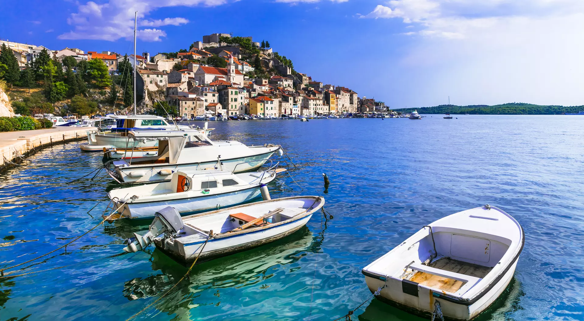 Scenic view of boats moored along a calm blue sea, with a charming coastal town in the background and a clear sky.