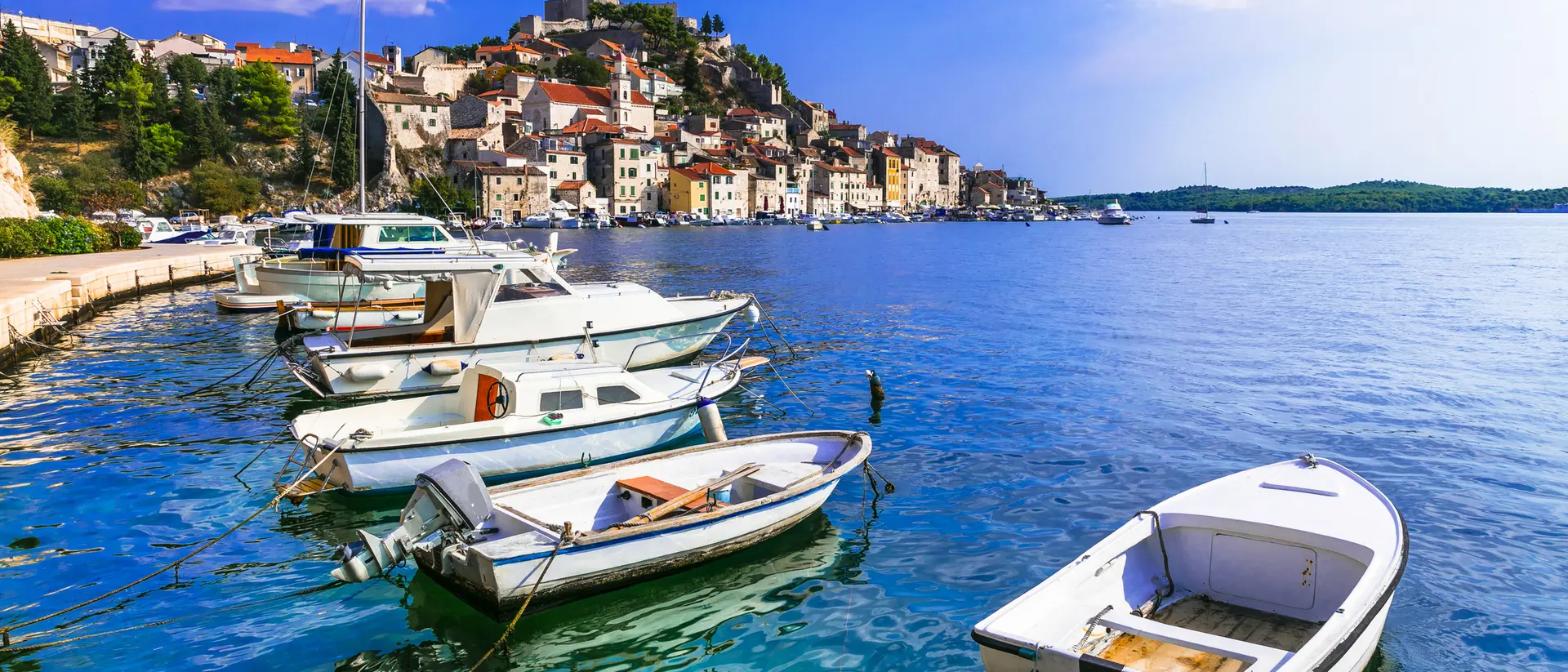 Scenic view of boats moored along a calm blue sea, with a charming coastal town in the background and a clear sky.