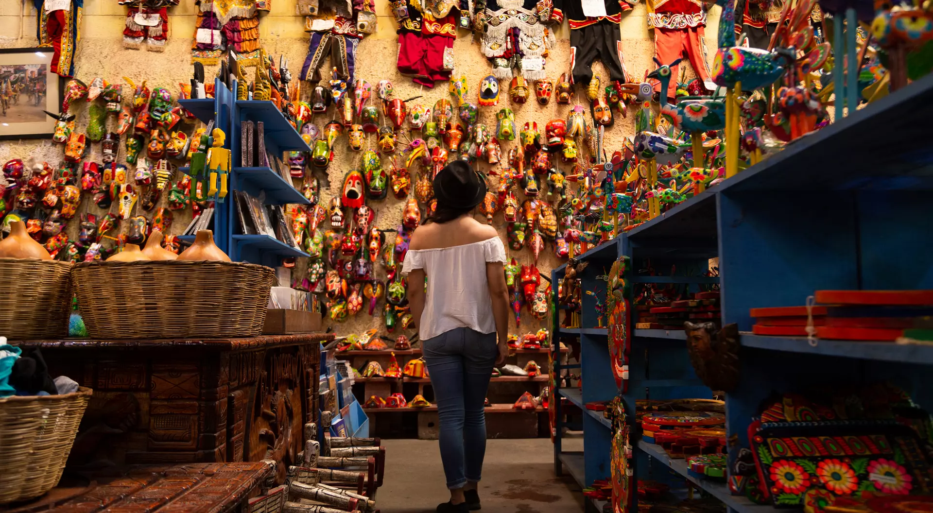 A person stands in a colorful artisan shop, surrounded by vibrant crafts and decorations on the walls and shelves.