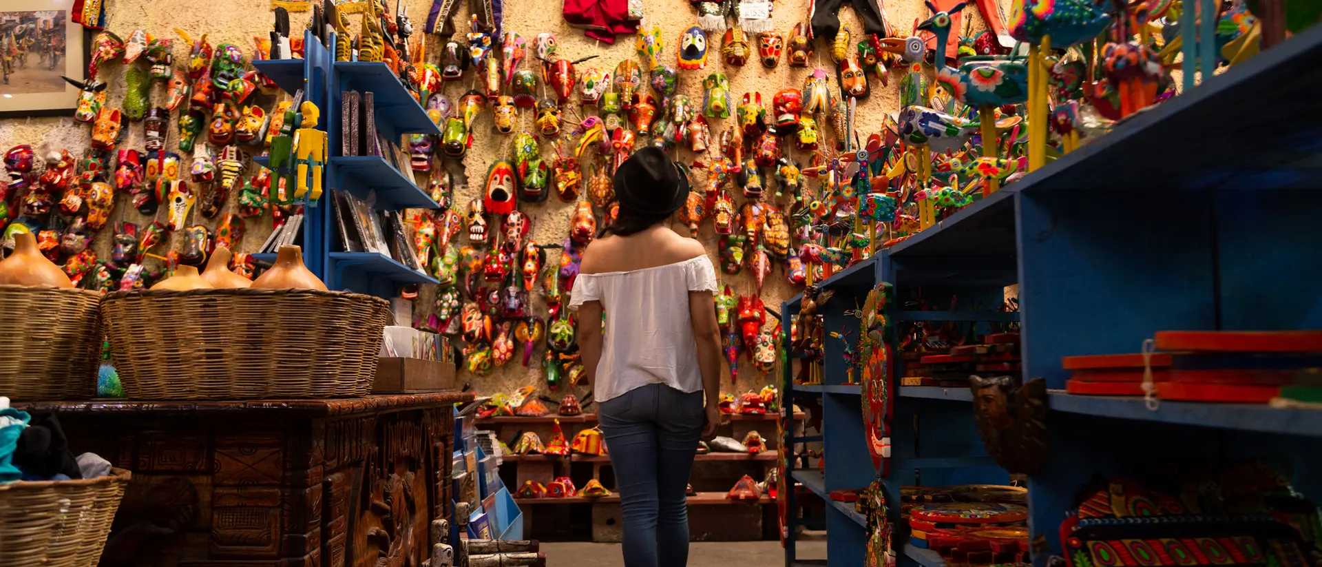 A person stands in a colorful artisan shop, surrounded by vibrant crafts and decorations on the walls and shelves.