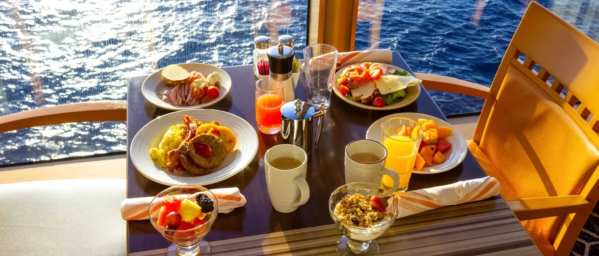 A table set with various breakfast dishes and drinks, overlooking the ocean through large windows.