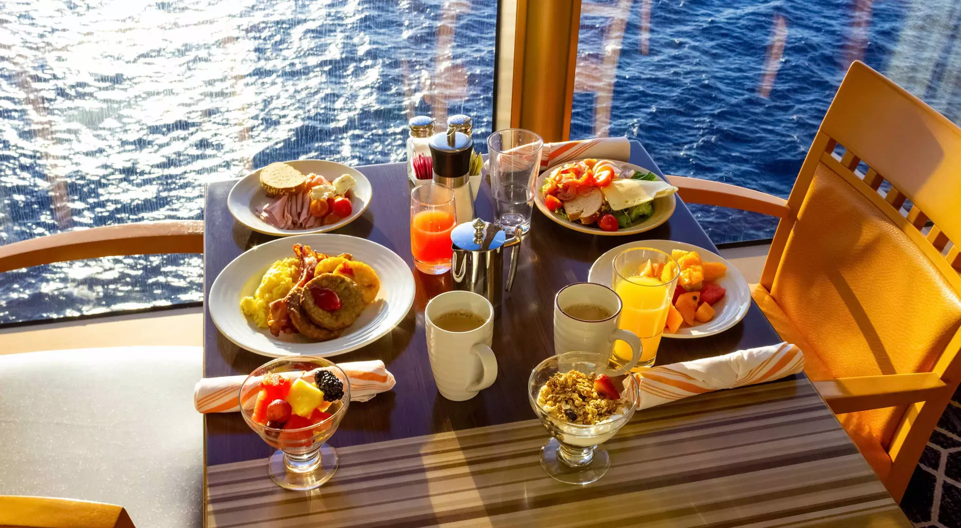 A table set with various breakfast dishes and drinks, overlooking the ocean through large windows.