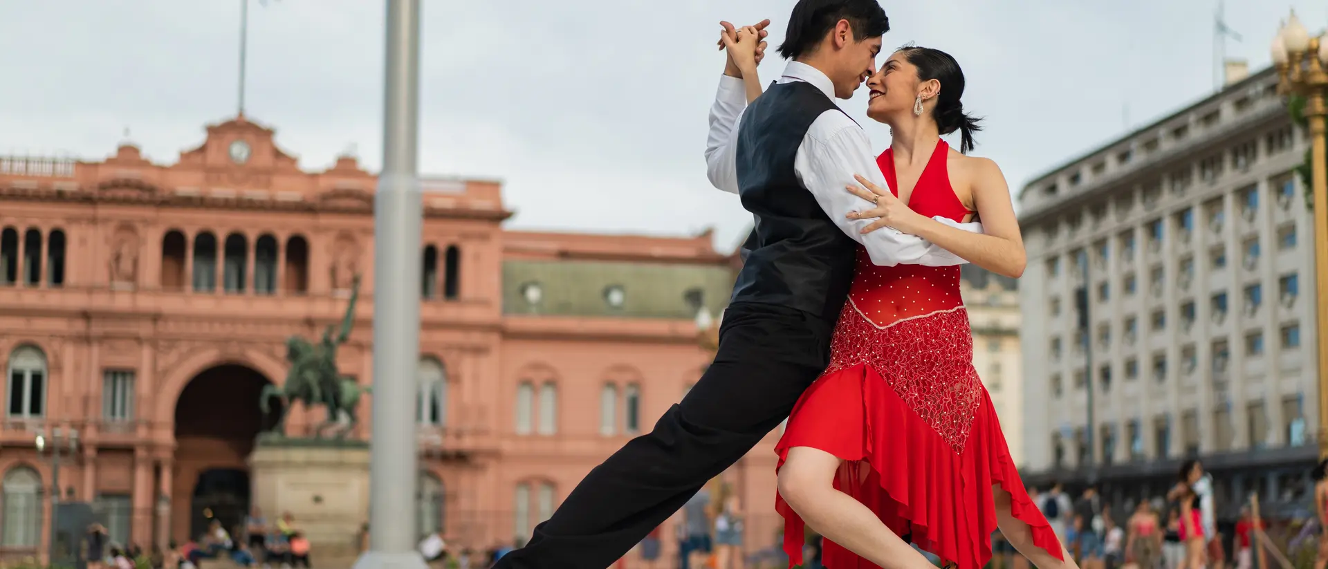 A couple dances tango in front of a historic building, showcasing their passion and elegance in a vibrant outdoor setting.