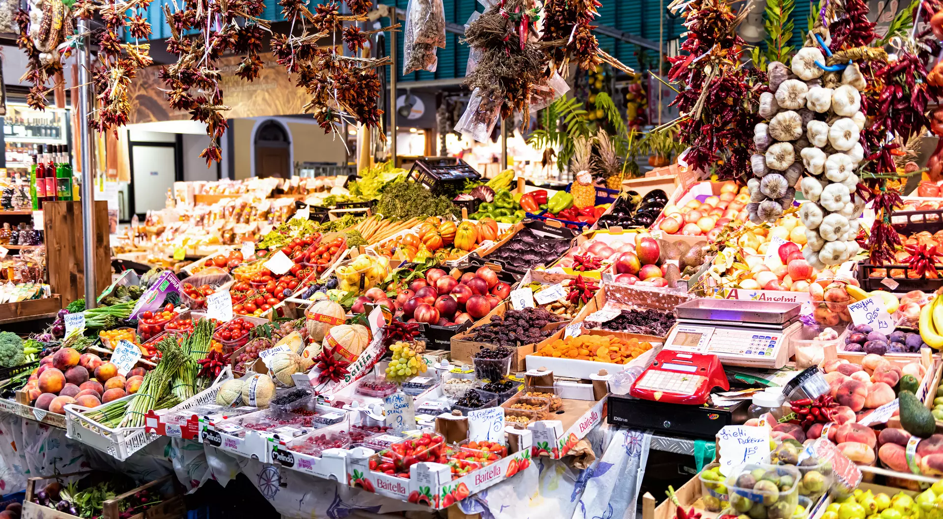 Vibrant market scene filled with colorful fruits, vegetables, and hanging spices displayed on various stalls.