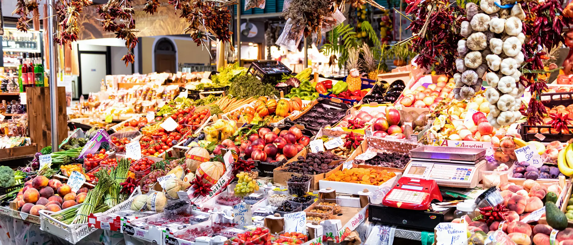 Vibrant market scene filled with colorful fruits, vegetables, and hanging spices displayed on various stalls.