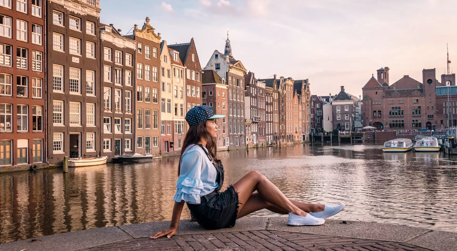 A person sits by a canal in Amsterdam, surrounded by historic buildings at sunset.