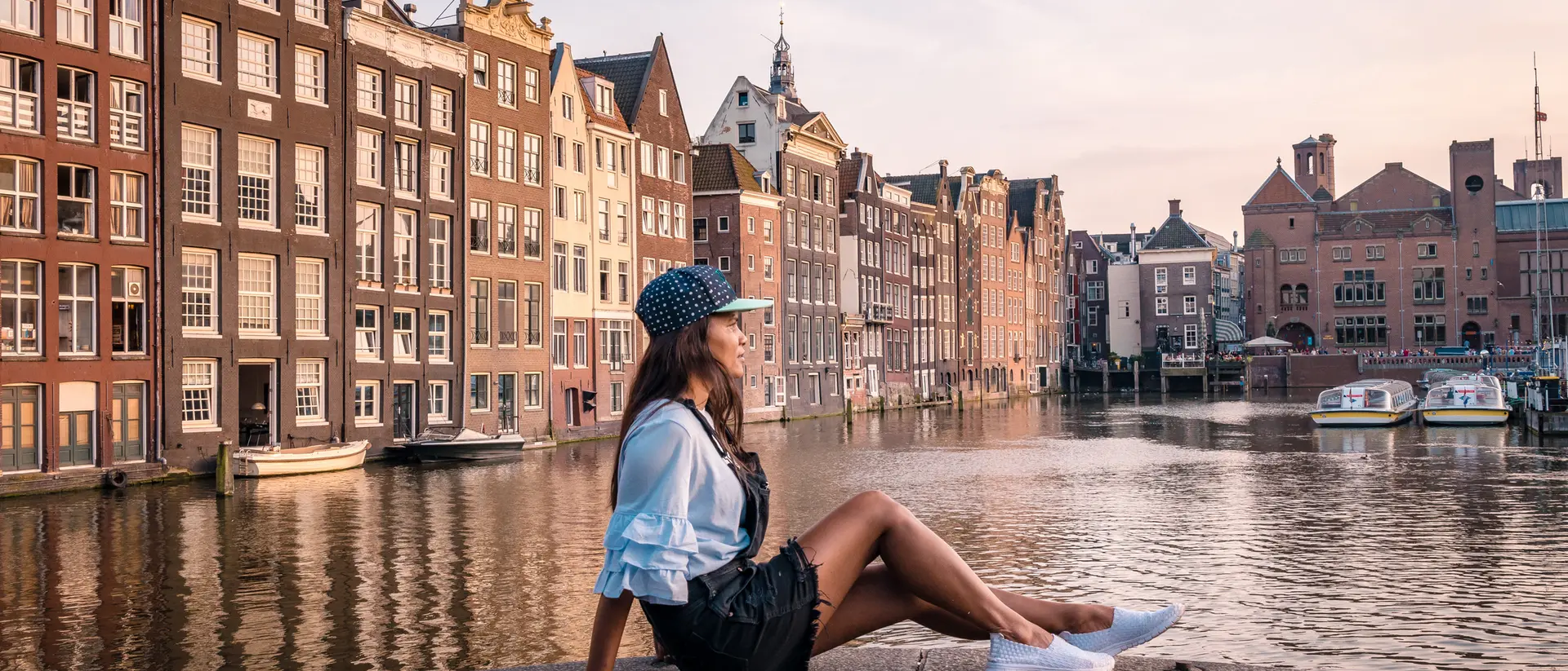 A person sits by a canal in Amsterdam, surrounded by historic buildings at sunset.
