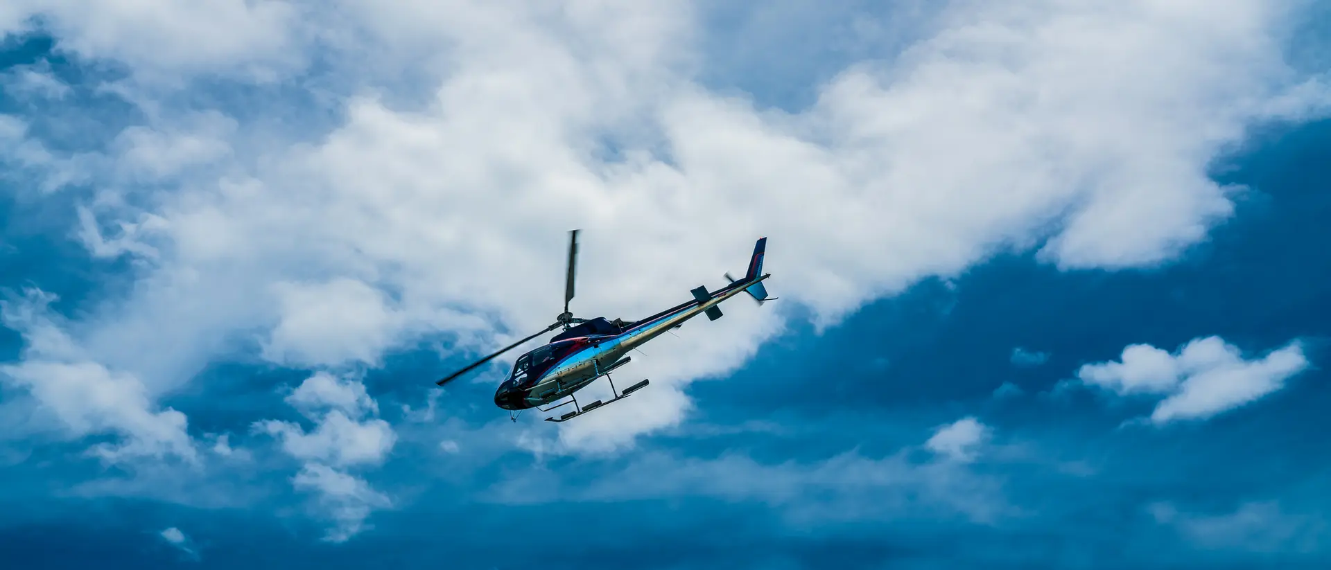 A helicopter flying against a backdrop of blue sky and fluffy white clouds.