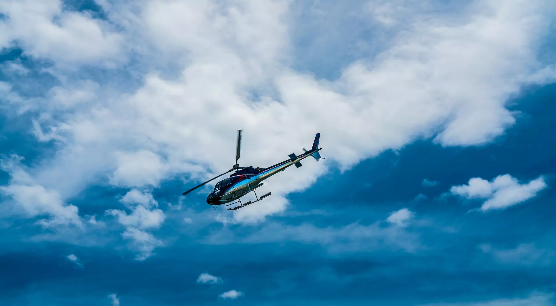 A helicopter flying against a backdrop of blue sky and fluffy white clouds.