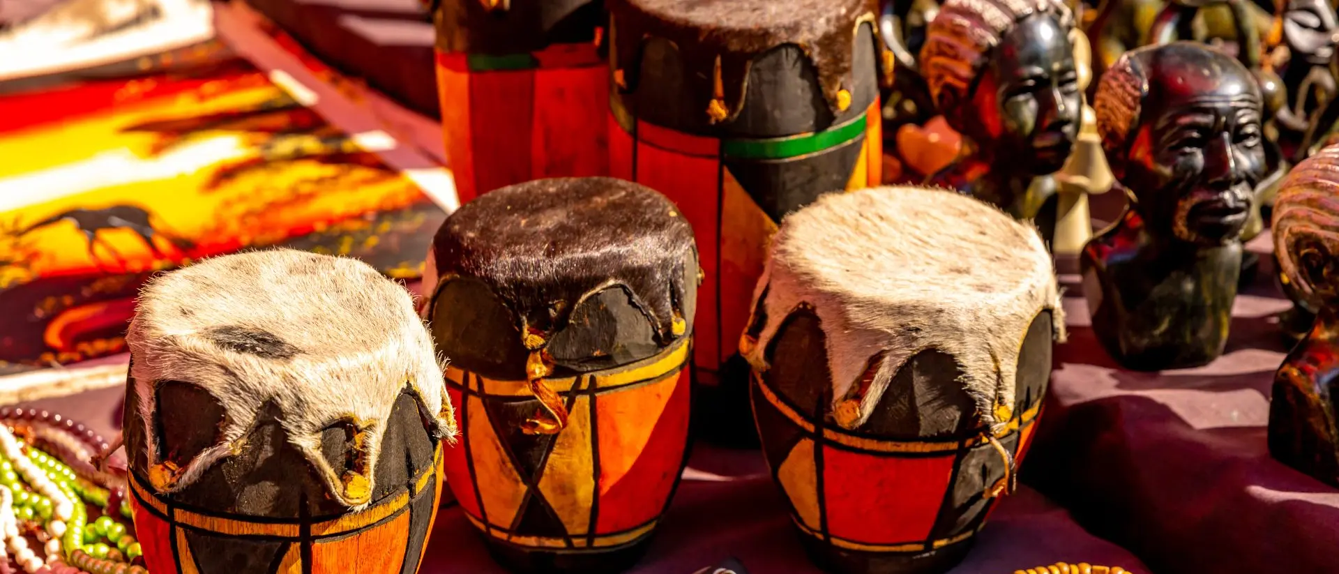 Colorful handmade drums with fur tops surrounded by beads and carved figures at a market.