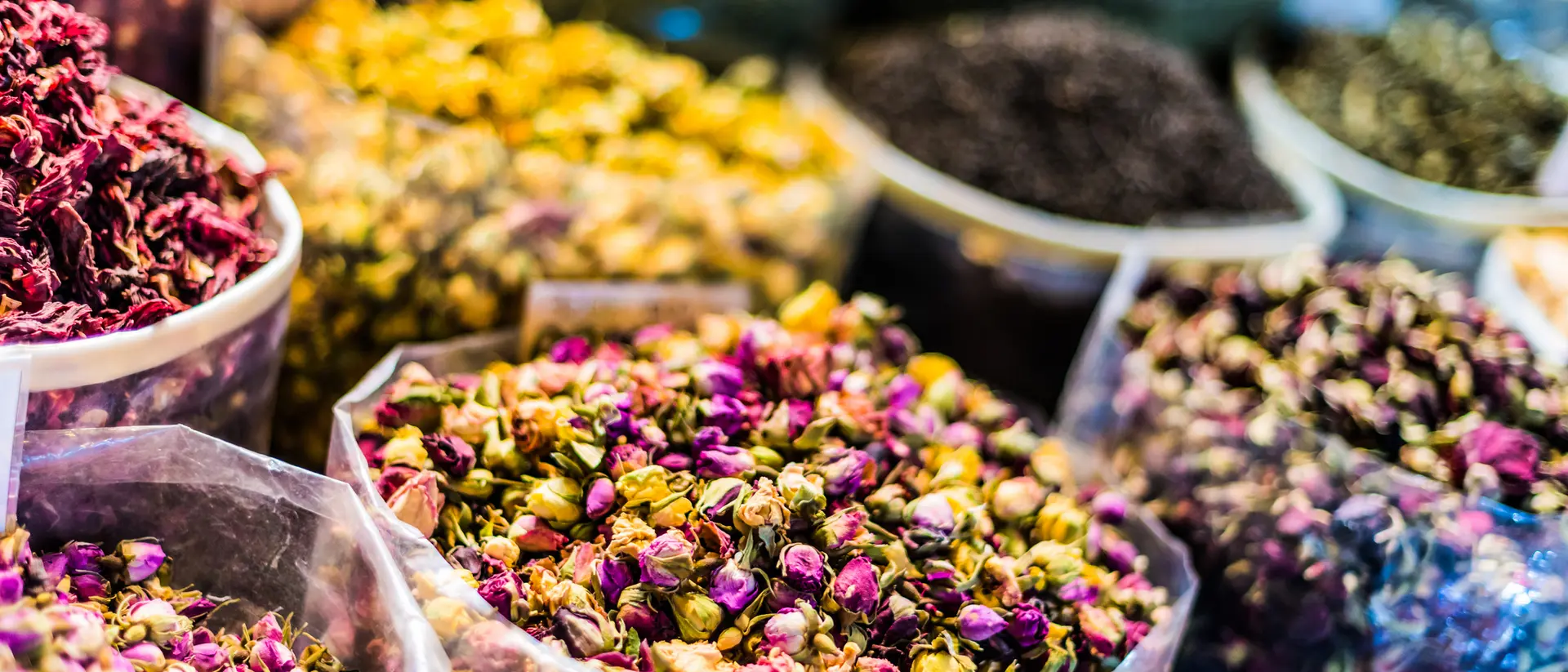 Colorful dried flower petals in transparent containers at a market, showcasing a variety of textures and hues.