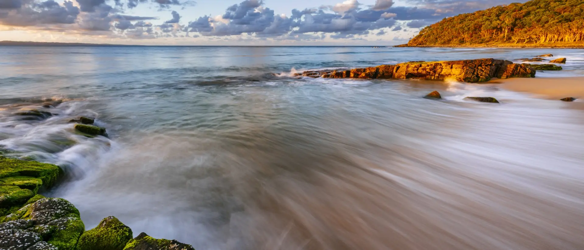 Water crests the shoreline at sunset
